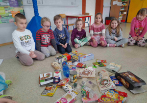 Dzieci siedzą przed zgromadzonymi opakowaniami po produktach spożywczych